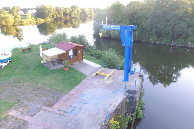 Kranstruktur Holzhaus am Ufer eines ruhigen Gewässers, mit einer blauen Kranstruktur im Hintergrund.